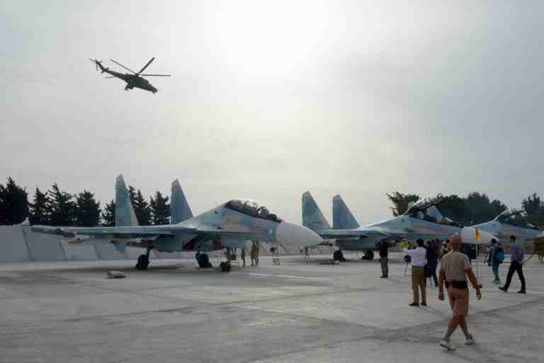 Journalists film Su-30 jets parked at Hemeimeem airbase, Syria, on Thursday, Oct. 22, 2015, as  Mi 24 helicopter gunship flies overhead. Since early morning, Russian combat jets have been taking off from this base in western Syria, heading for missions. (AP Photo/Vladimir Kondrashov) 2