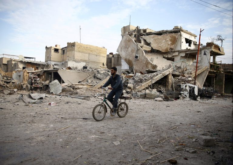 A young man rides bicycle near damaged houses in the besieged town of Douma, Eastern Ghouta, Damascus, Syria February 20, 2018. REUTERS/Bassam Khabieh