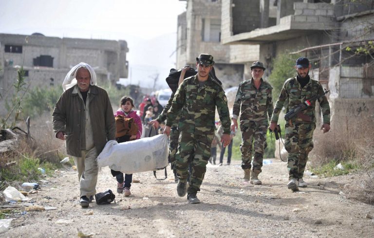This photo released by the Syrian official news agency SANA, shows Syrian government soldiers, helping civilians who fled from fighting between the Syrian government forces and insurgents, through the Wafideen crossing in eastern Ghouta, a suburb of Damascus, Syria, Thursday, March 22, 2018. Syrian troops have recently taken control of about 80 percent of eastern Ghouta from rebel forces.(SANA via AP)