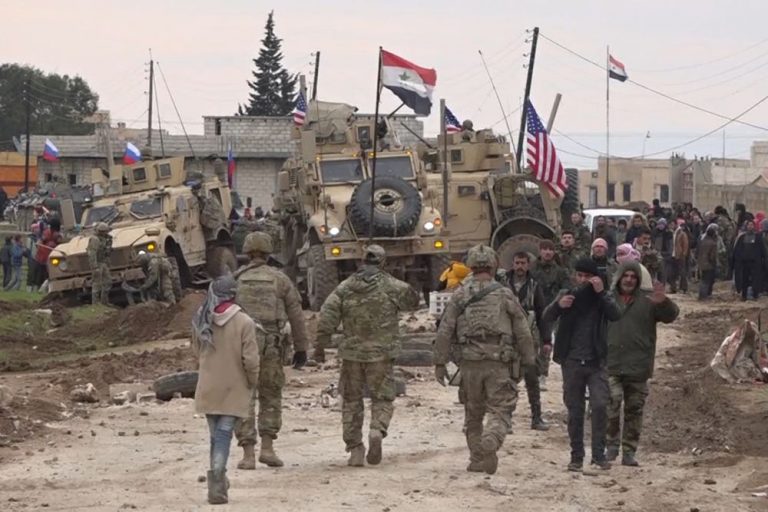 In this frame grab from video, Russian, Syrian and others gather next to an American military convoy stuck in the village of Khirbet Ammu, east of Qamishli city, Syria, Wednesday, Feb. 12, 2020. Syrian media and activists say a Syrian was killed and another wounded in a rare clash between American troops and a group of government supporters in northeast Syria. (AP Photo)
