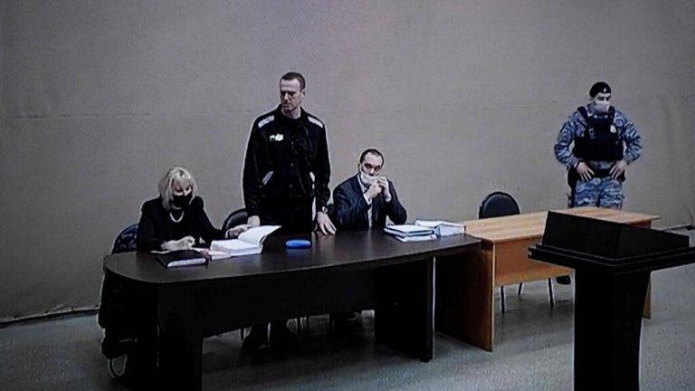 A photograph taken from a TV screen during live broadcast of the court hearing at the penal colony N2 shows Kremlin critic Alexei Navalny (C) during the court hearing at the penal colony N2, on the first day of his new trial, in the town of Pokrov on February 15, 2022. - A new trial against jailed Kremlin critic Alexei Navalny began on February 15, 2022 inside the prison colony where he serves a two-and-a-half year prison term for violating parole, in a case that could see his sentence extended by more than a decade. (Photo by Alexander NEMENOV / AFP)